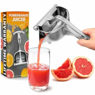 Hand squeezing juice from pomegranate using a manual juicer into a glass.